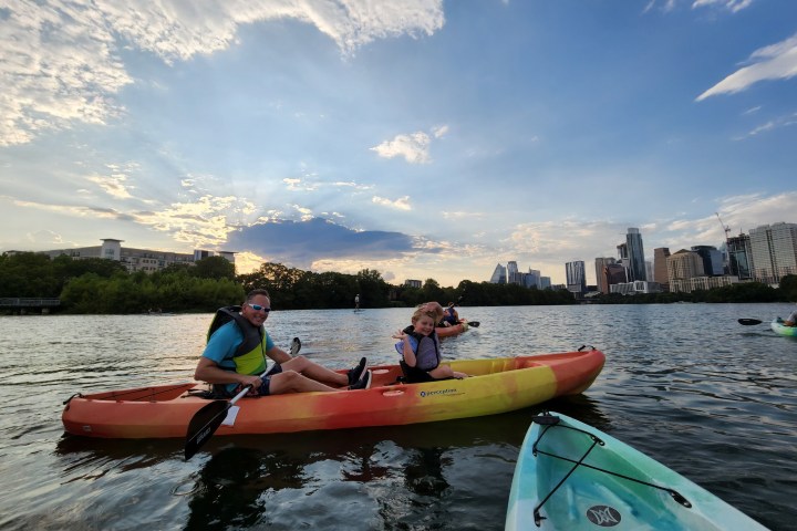 People kayaking on a lake with a city skyline and cloudy sky in the background.