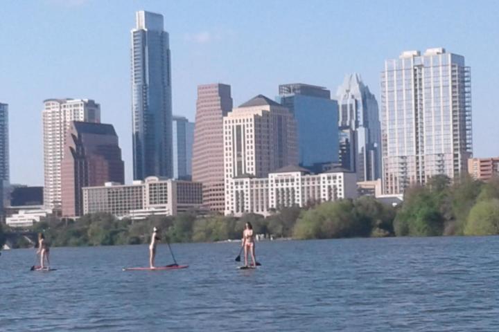People paddleboarding on a river with a city skyline in the background.