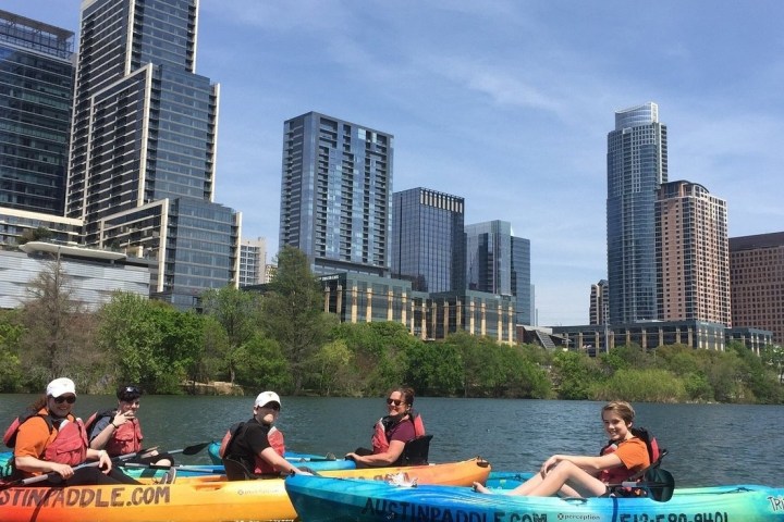 People kayaking on a river with a city skyline in the background.