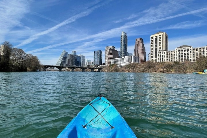 View from a kayak on a river with a city's skyline and a bridge in the background.