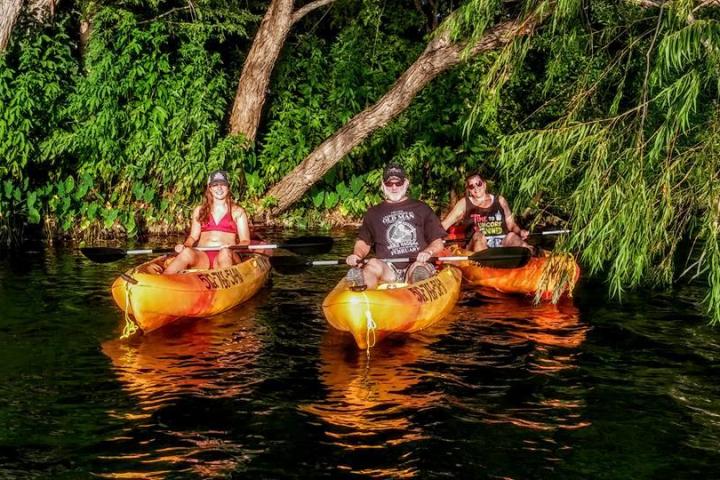 Three people in kayaks on a river, with trees and foliage in the background.