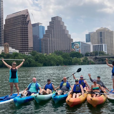Group of people on kayaks and paddleboards with city skyline in the background.