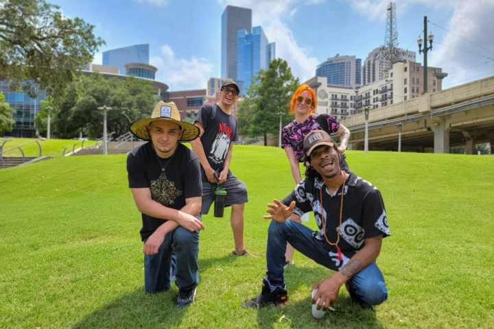 Four people posing on grass in front of city skyline, with buildings in the background.