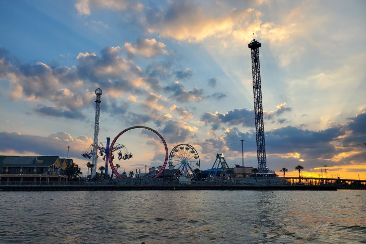 Amusement park rides silhouetted against a sunset sky with clouds over a body of water.