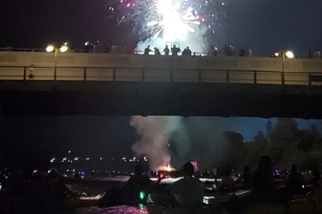 Fireworks above a bridge with people watching, silhouetted against the night sky.
