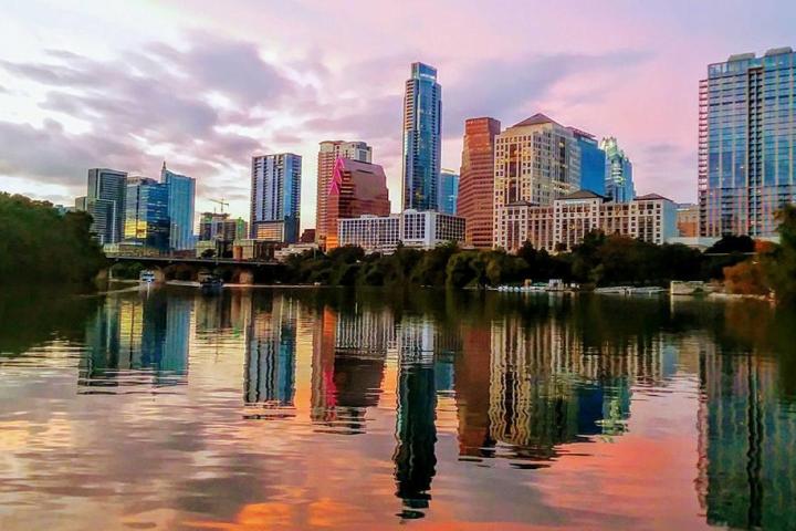 City skyline reflected in calm water during sunset with colorful sky and clouds.