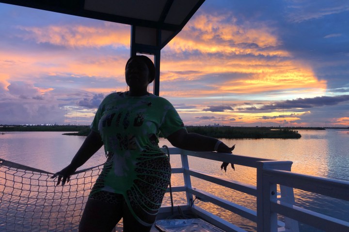 Silhouette of a person on a deck against a vibrant sunset over a lake.